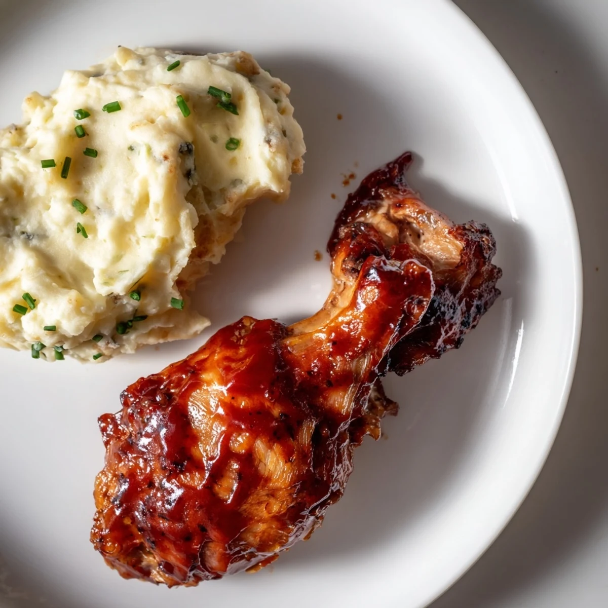 Honey BBQ chicken thighs glistening on a plate, alongside fluffy garlic mashed potatoes for a hearty dinner.