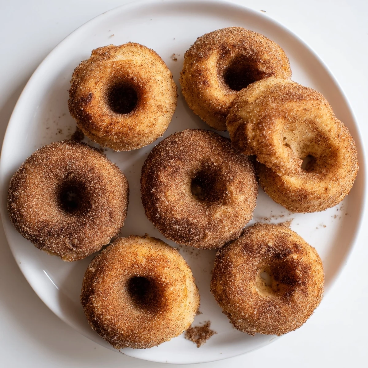 Overhead view of Air Fryer Cinnamon Sugar Donuts arranged on a rustic plate, coated in cinnamon sugar and ready to be enjoyed with milk.