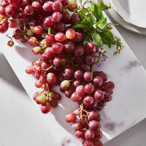 Juicy red and green grapes spilling elegantly over a wooden board edge, ready to serve this fresh snack.