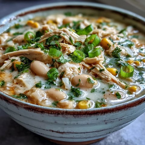 A bowl of creamy White Chicken Chili garnished with cilantro and cheese, served with lime wedges and tortilla chips.