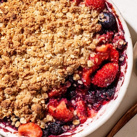 Warm, comforting Summer Berry Crisp: juicy berries visible beneath a lightly browned topping.