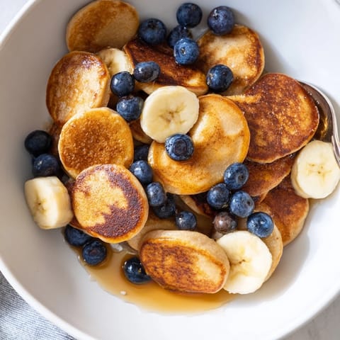 Bite-sized, fluffy mini pancake cereal topped with honey and sliced bananas for breakfast.  