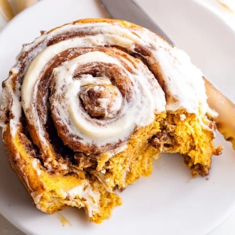 Frosted pumpkin cinnamon rolls sit in a ceramic baking dish, showcasing their golden swirls and gooey filling.