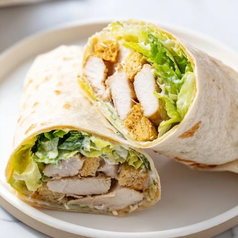 The Caesar Chicken Salad Wrap showcases juicy sliced chicken and crunchy croutons on a wooden cutting board.  