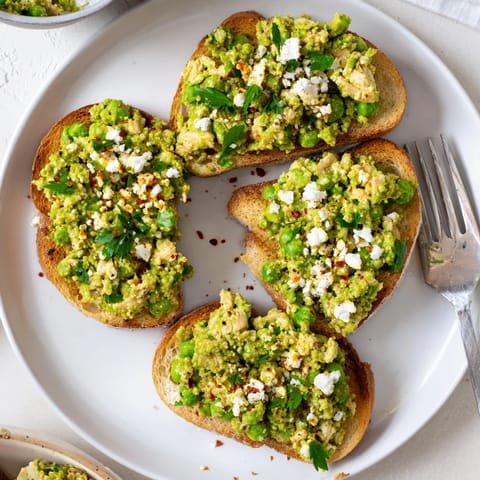 Savory smashed pea and chicken toast piled high with herbs and chili flakes on golden toasted bread.