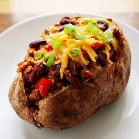 Steaming Chili-Style Baked Potatoes, a warm and colorful bowl bursting with chili and cheesy toppings for dinner.
